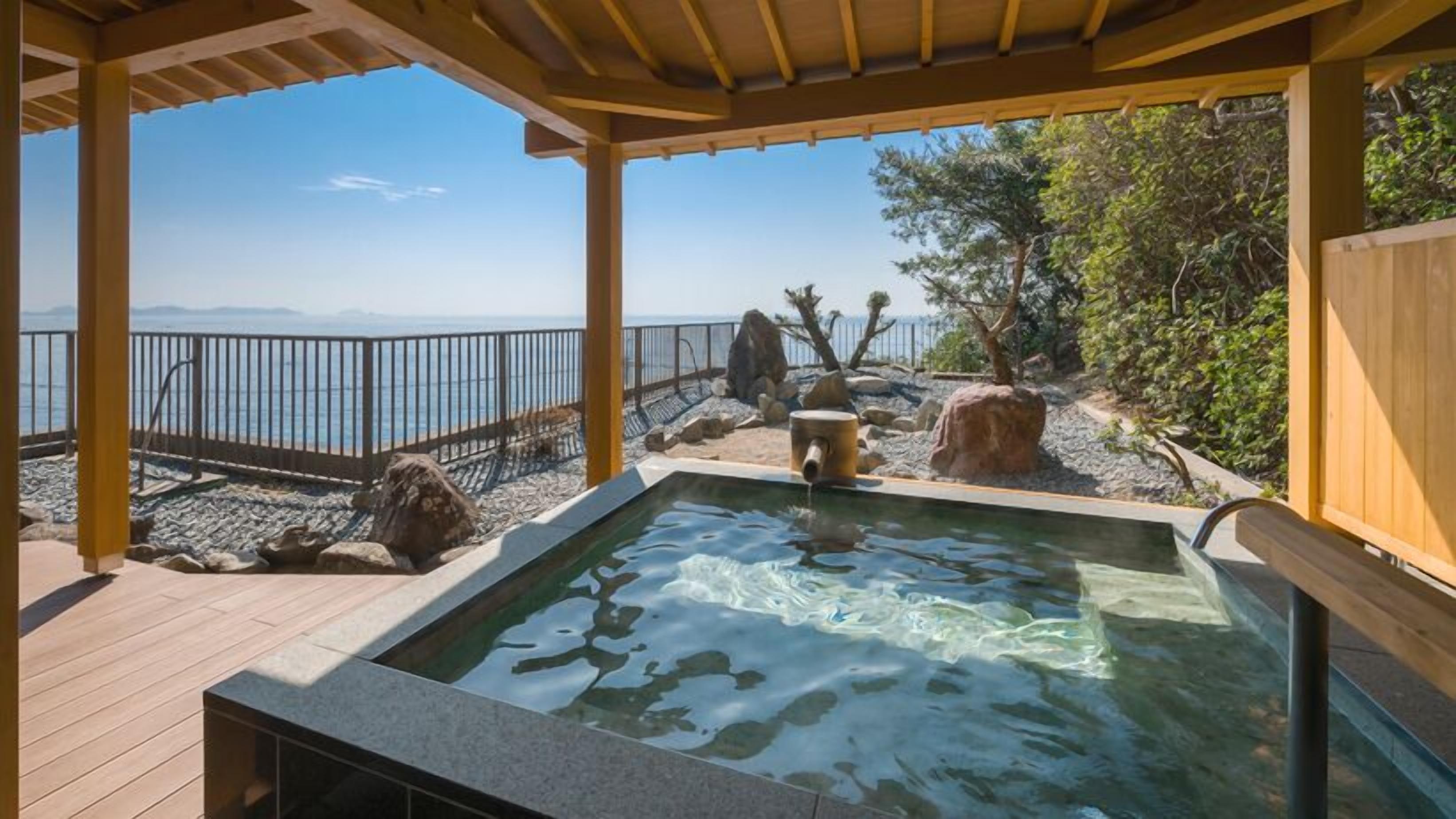 A hot tub with a view of the sea, surrounded by rocks and trees.