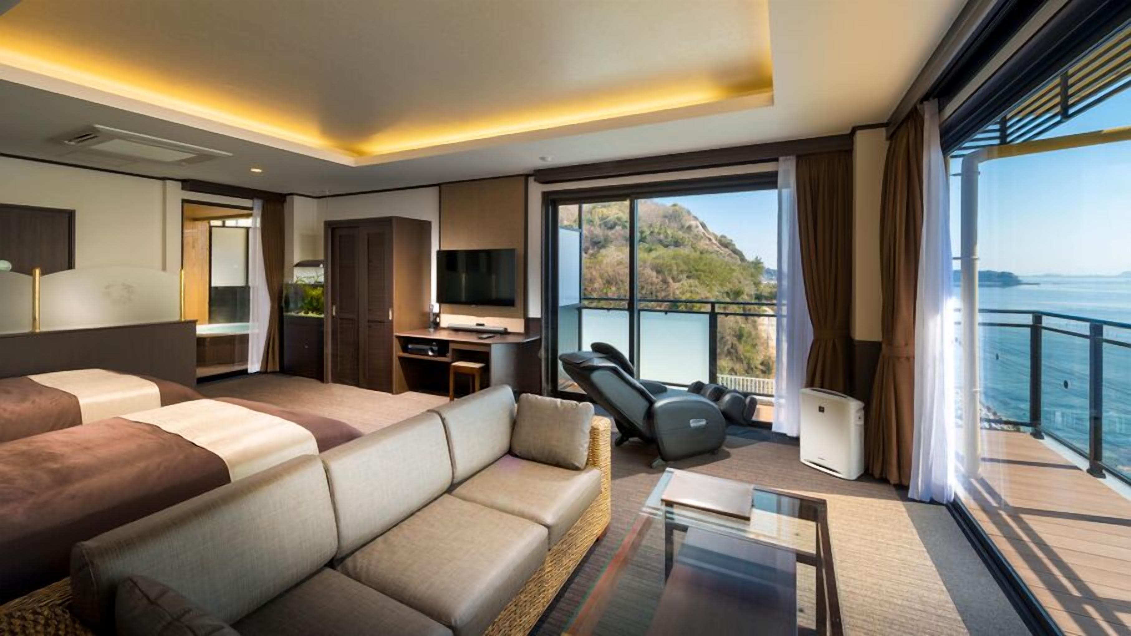 Ein modernes Hotelzimmer mit einem großen Bett, einer Couch, einem Schreibtisch mit Fernseher und einem Balkon mit Meerblick.