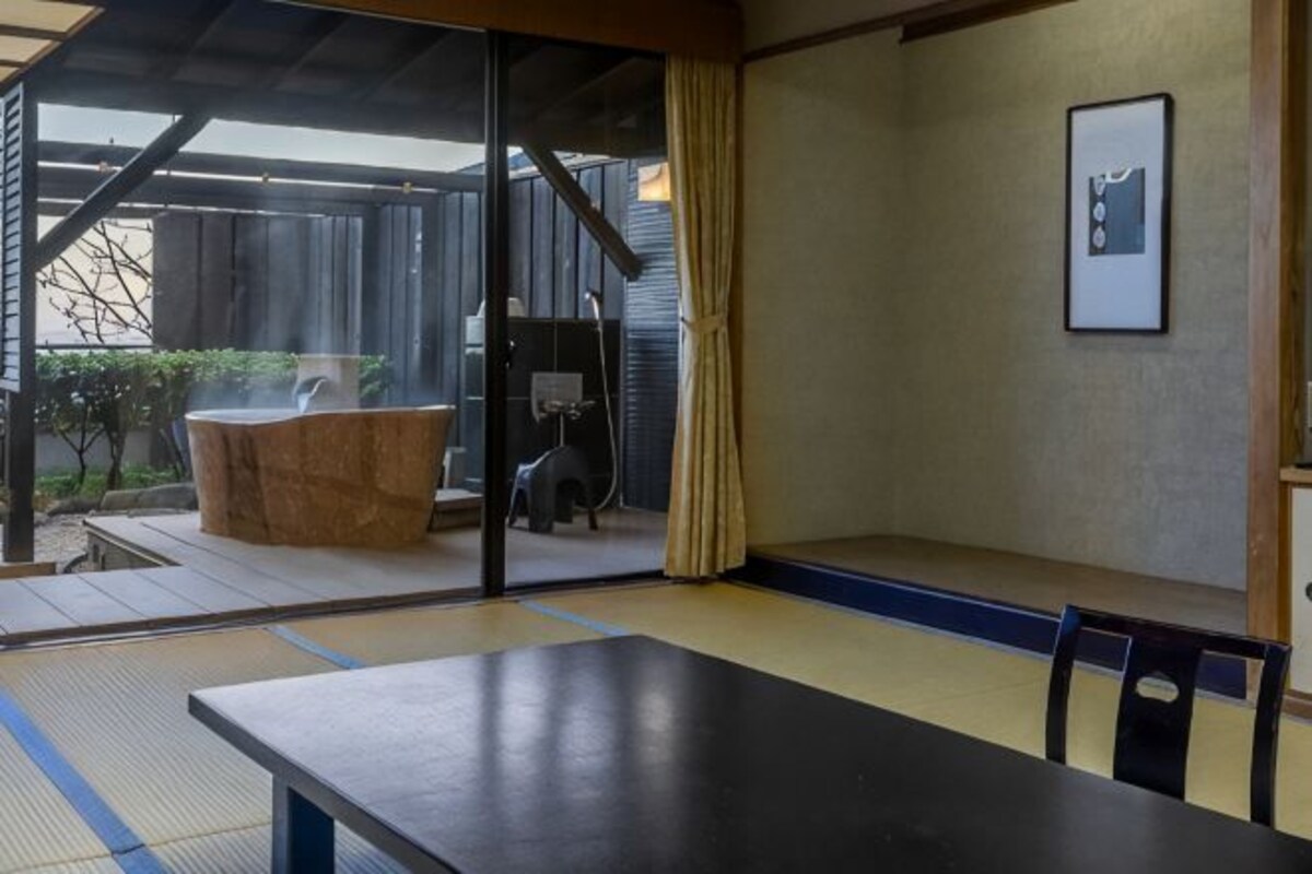 A tatami mat room with a sliding door leading to a garden area, a wooden table, and a framed picture on the wall.