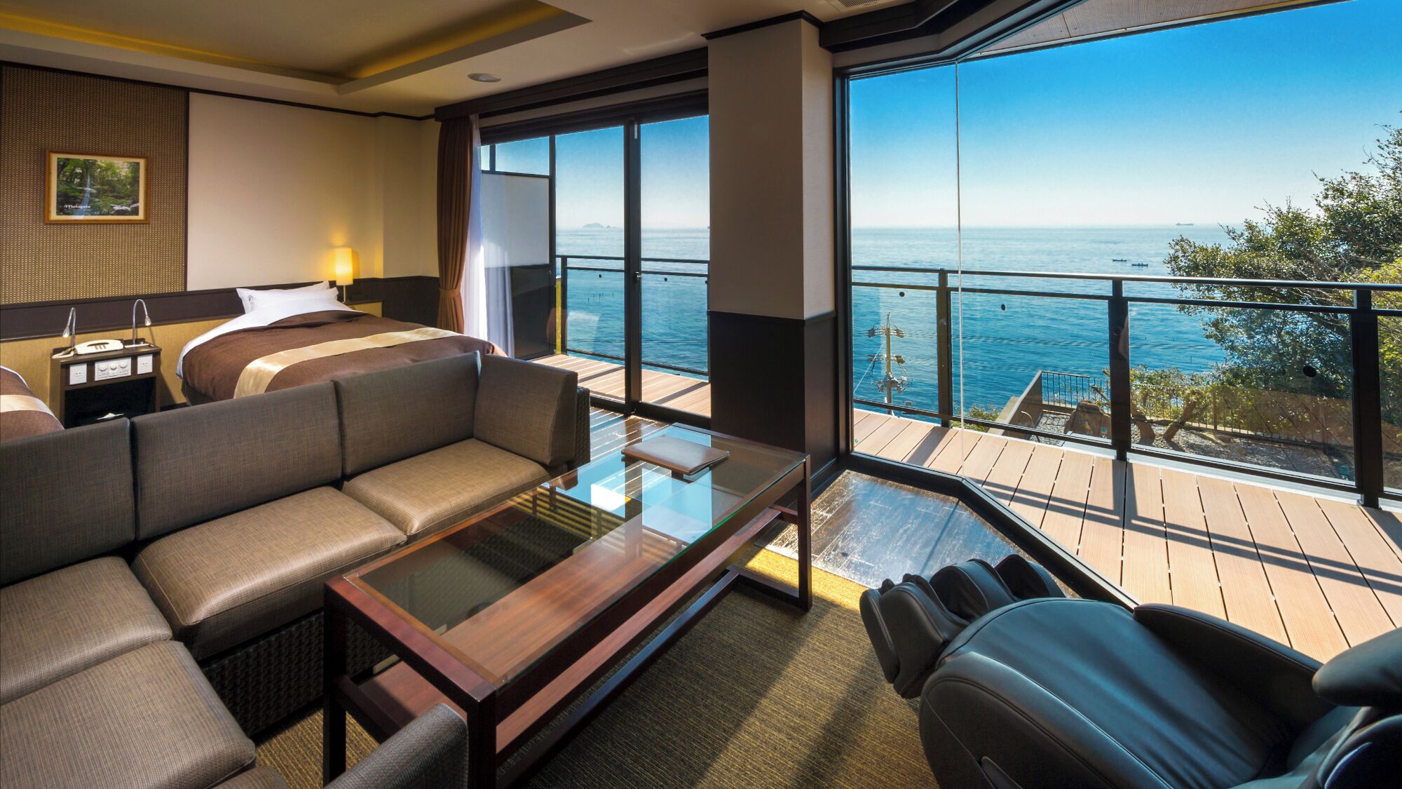 A modern hotel room with a large balcony, a sofa, a glass coffee table, and a bed.