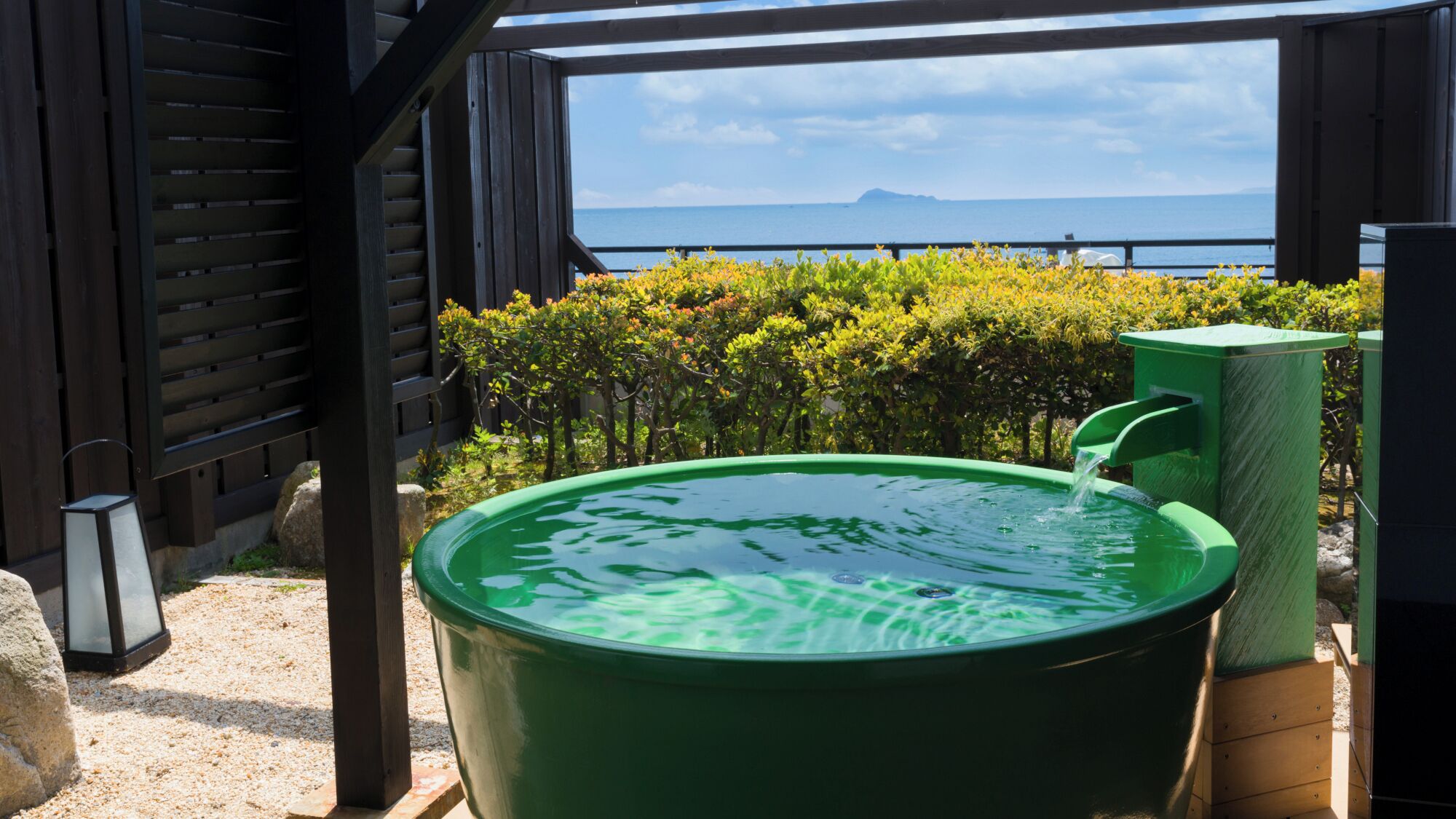 A green hot tub with a view of the sea and mountains.