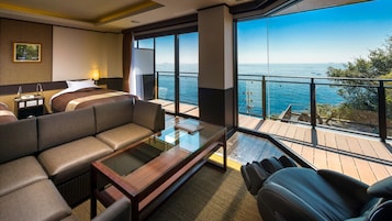 A modern hotel room with a large balcony, a sofa, a glass coffee table, and a bed with a headboard.