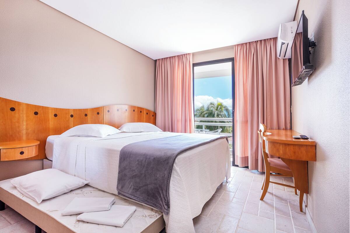 Une chambre d’hôtel équipée d’un lit, d’une table de chevet, d’un bureau, d’une chaise et d’un téléviseur fixé au mur.