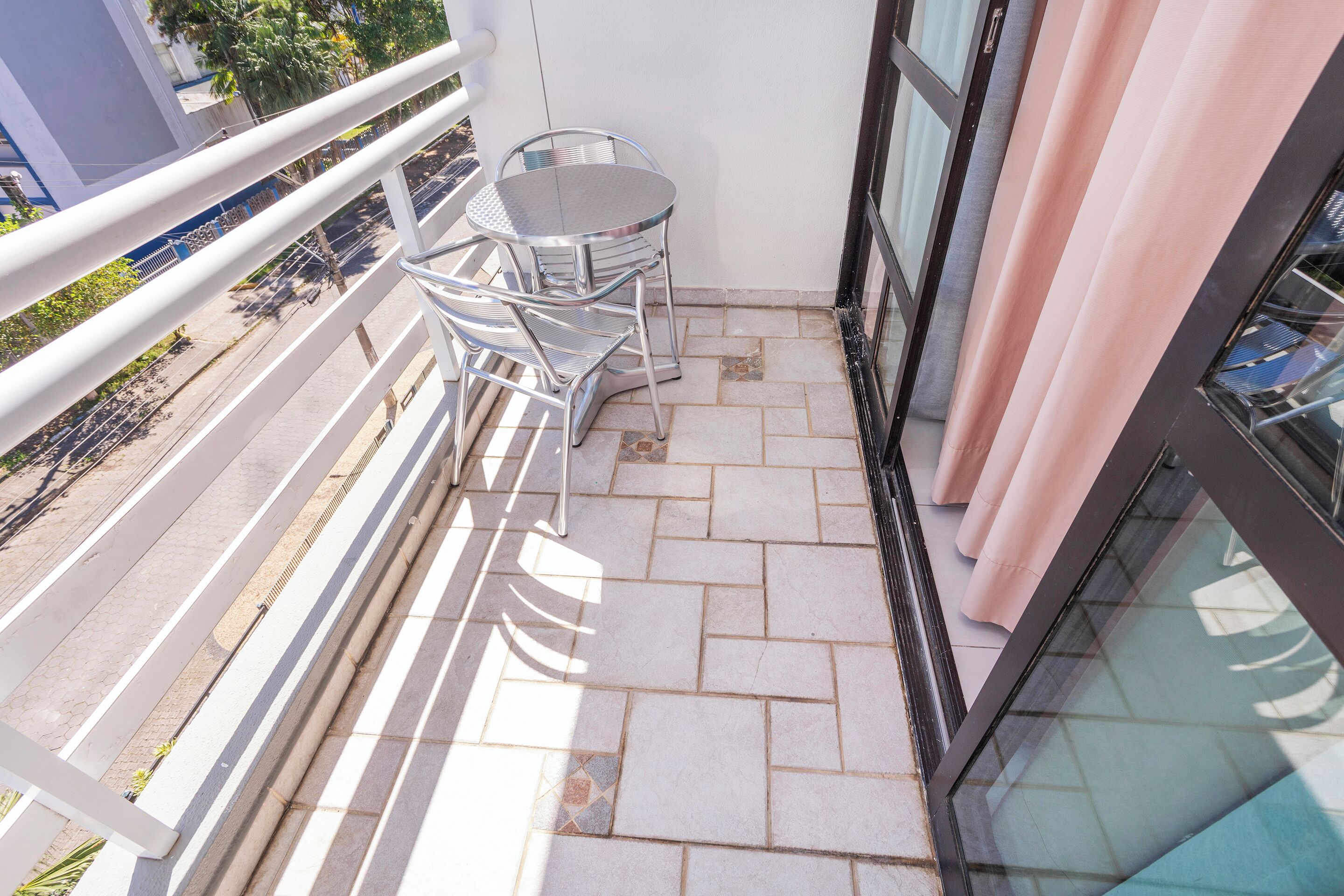 Uma varanda com mesa e cadeiras de metal, piso de azulejos e guarda-corpo.