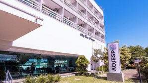 A modern building with a glass facade, balconies, and a sign reading 'AOJESP.' - Aojesp Hotel Colonia (Caraguatatuba)