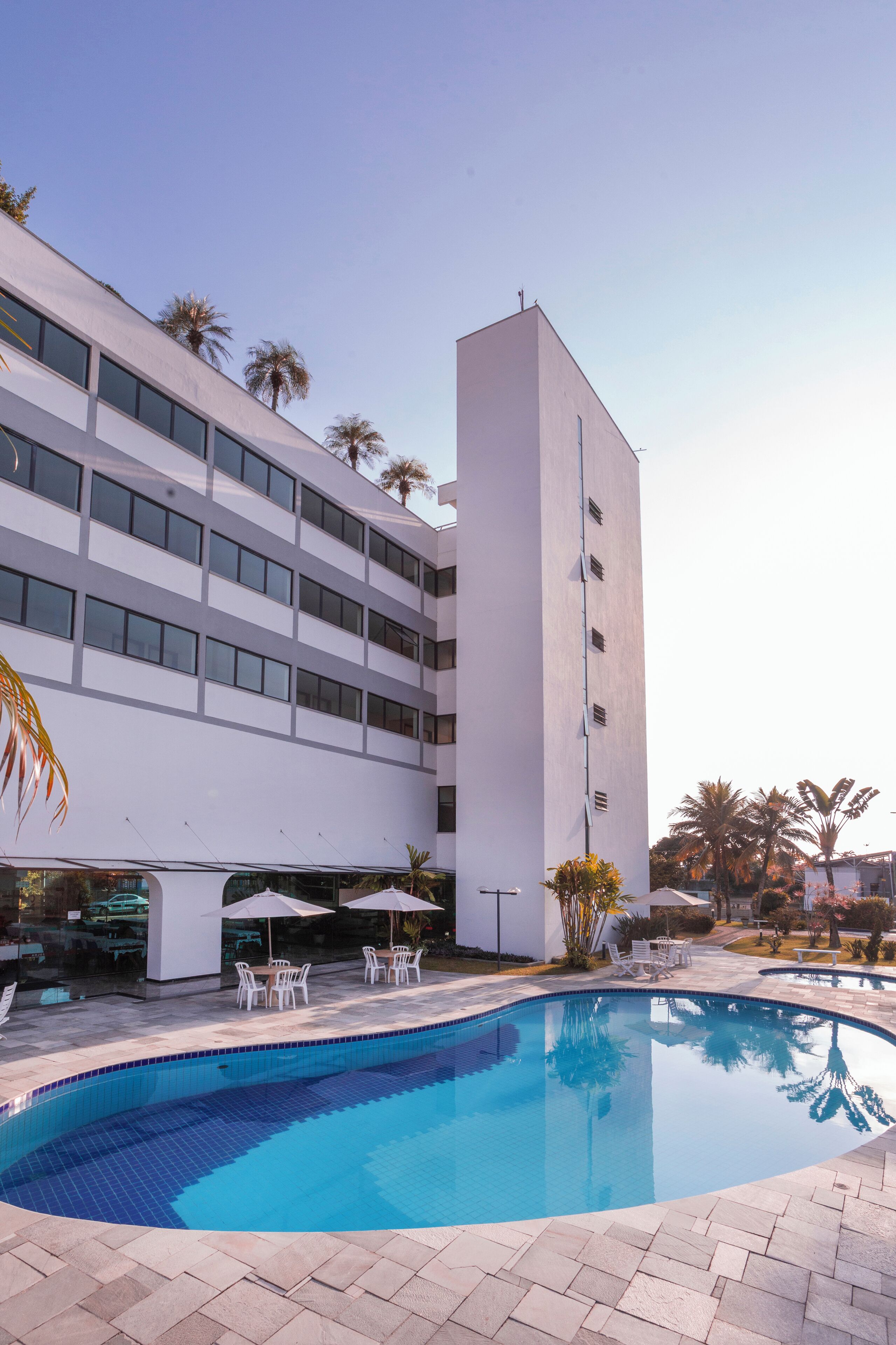 A modern hotel with a swimming pool, outdoor seating, and palm trees.
