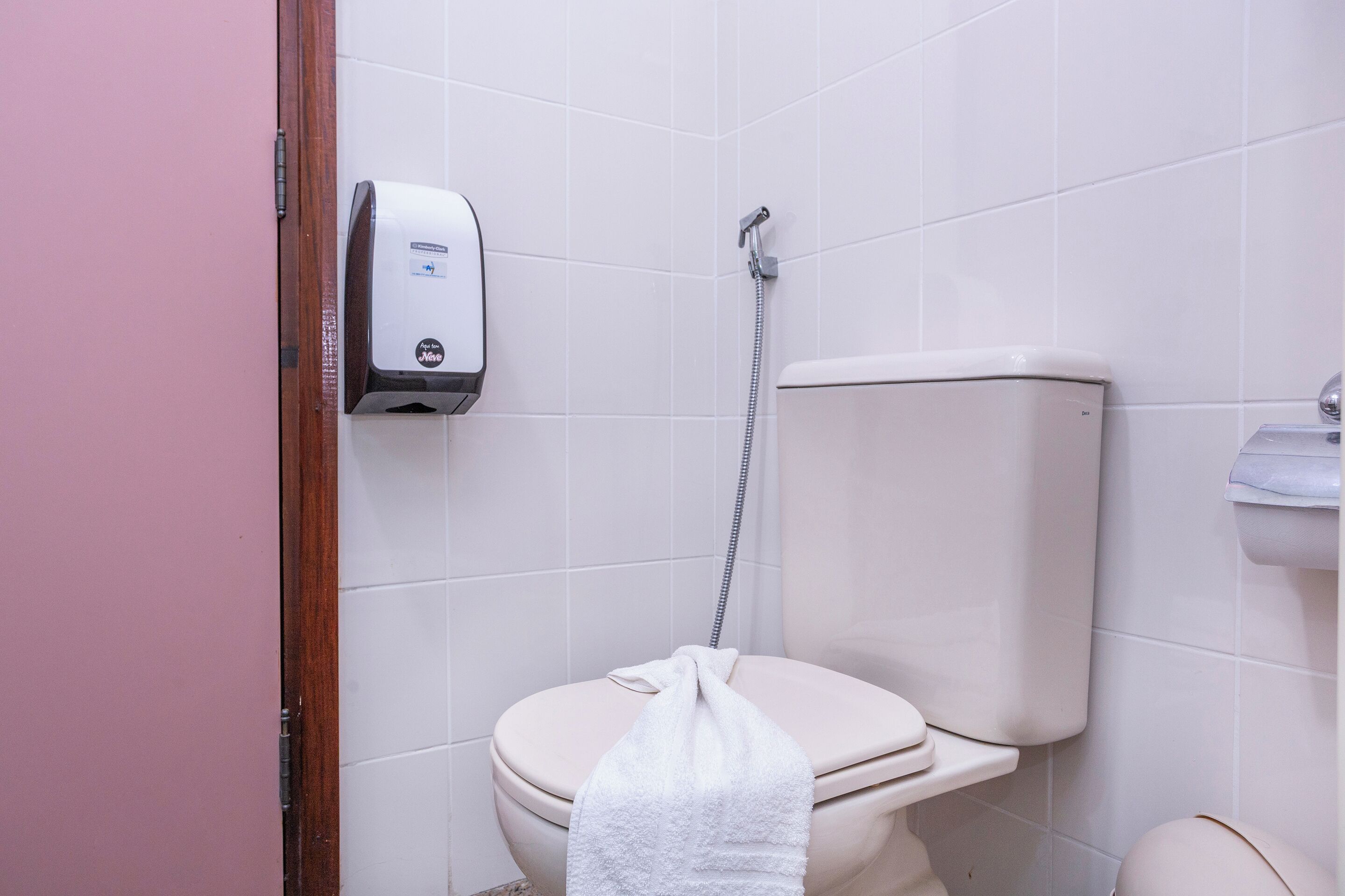 A bathroom with a toilet, a hand dryer, and a shower head.