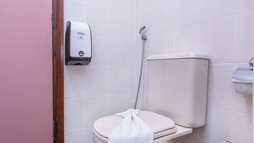 A bathroom with a toilet, a hand dryer, and a shower head.
