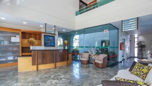 A hotel lobby with a reception desk, seating area, and a glass wall. - Aojesp Hotel Colonia (Caraguatatuba)