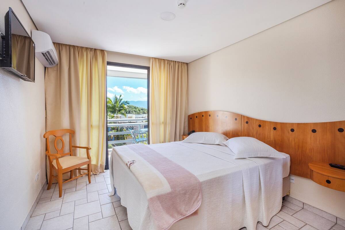 Une chambre d’hôtel avec un lit, une chaise, une télévision et une fenêtre avec des rideaux.