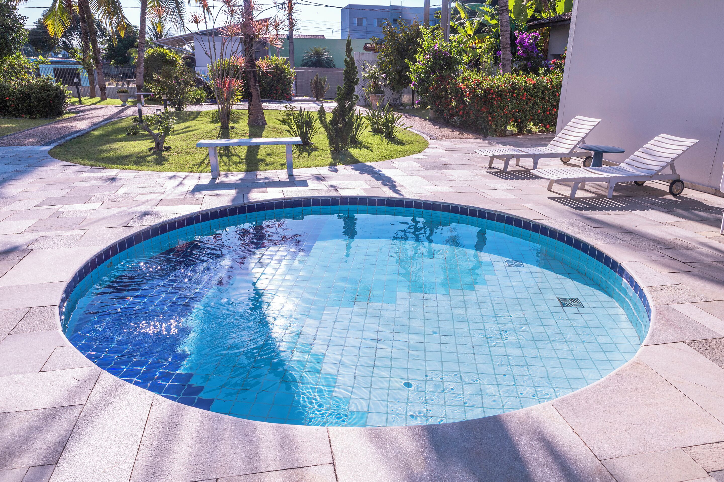 A swimming pool with tiled edges, surrounded by a paved area with lounge chairs and a small table.