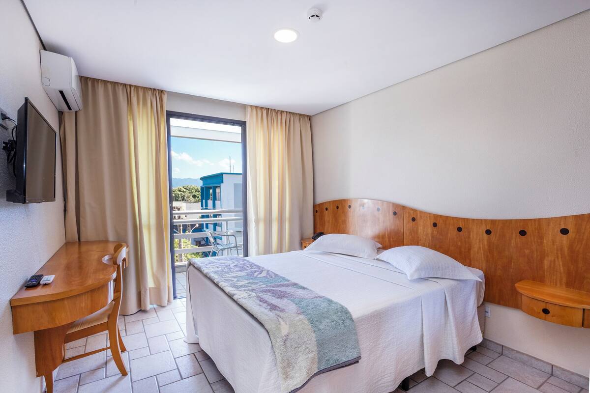 Une chambre d’hôtel avec un lit, un bureau, une chaise, une télévision et un balcon avec vue.
