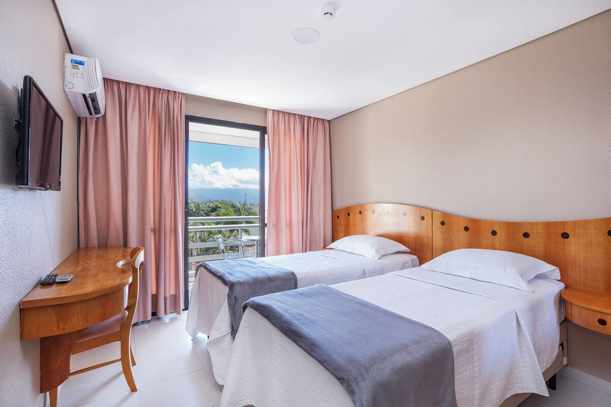 Une chambre d’hôtel avec deux lits, un bureau, une télévision et une fenêtre avec des rideaux.