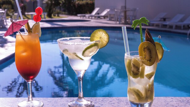 Three cocktails with garnishes by a poolside. - Aojesp Hotel Colonia (Caraguatatuba)