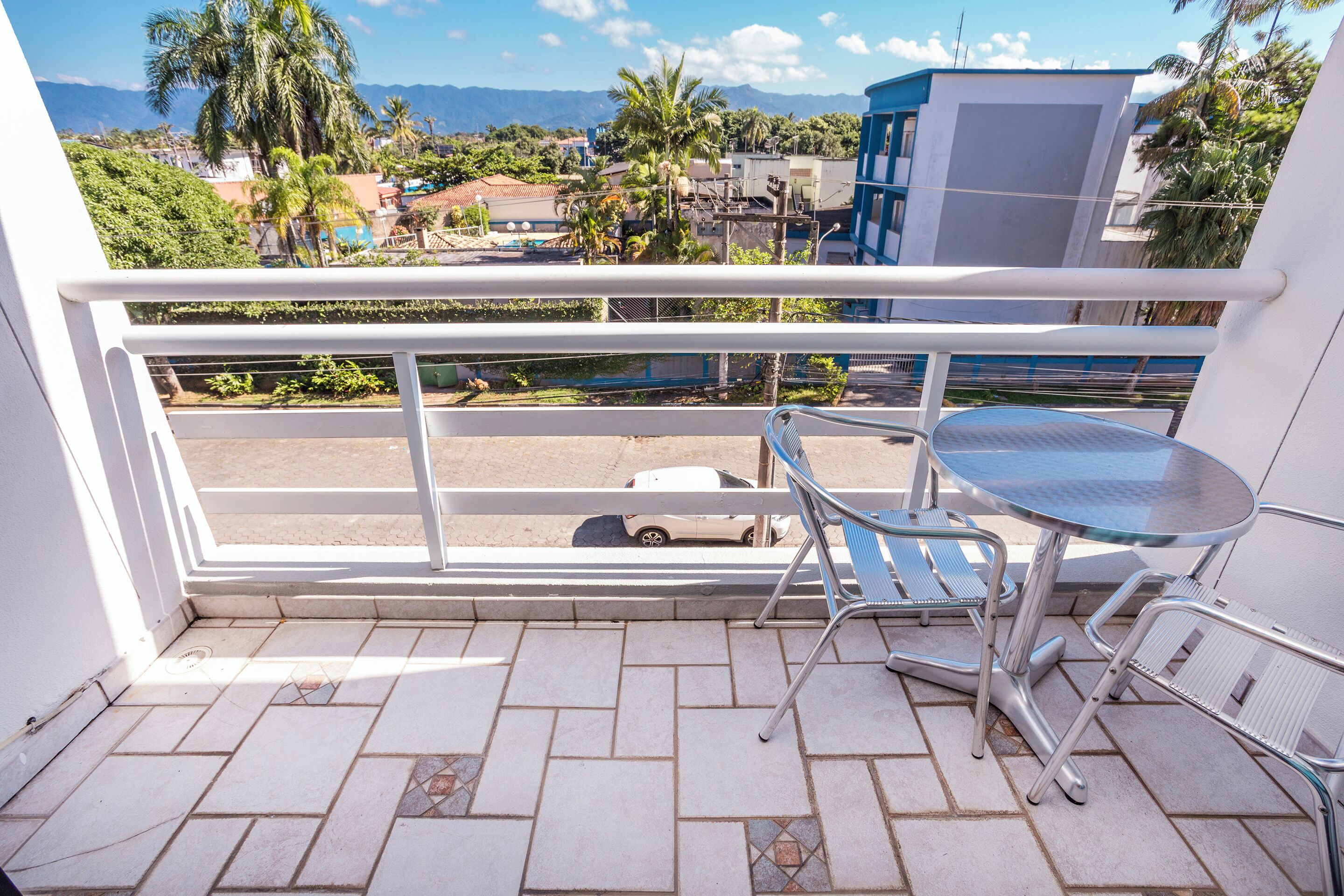 A balcony with a metal table and chairs, a view of a street with cars, and buildings in the background.
