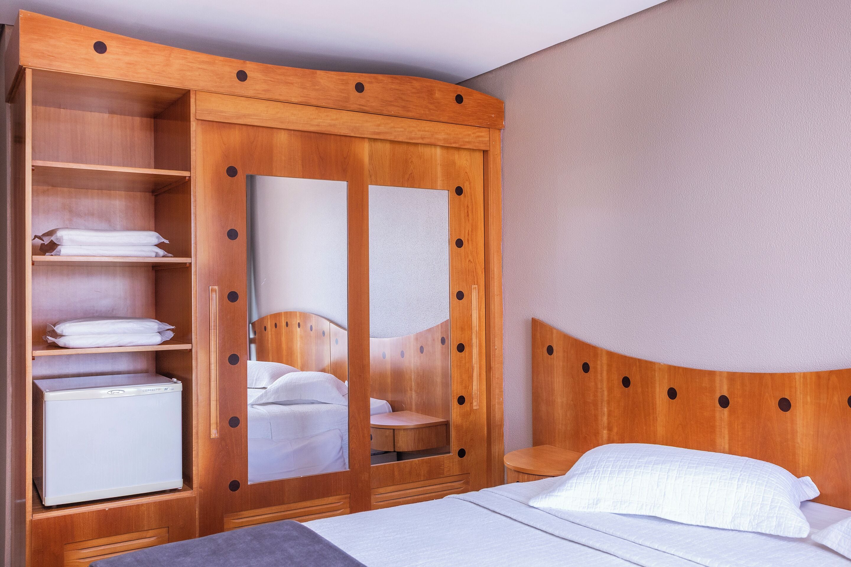A hotel room with a wooden wardrobe, a bed, and a small table.