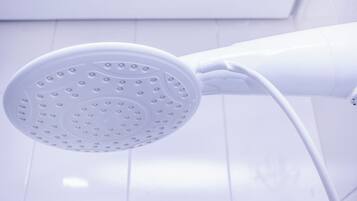 Un pommeau de douche blanc au design incurvé, fixé sur un mur recouvert de carreaux blancs.