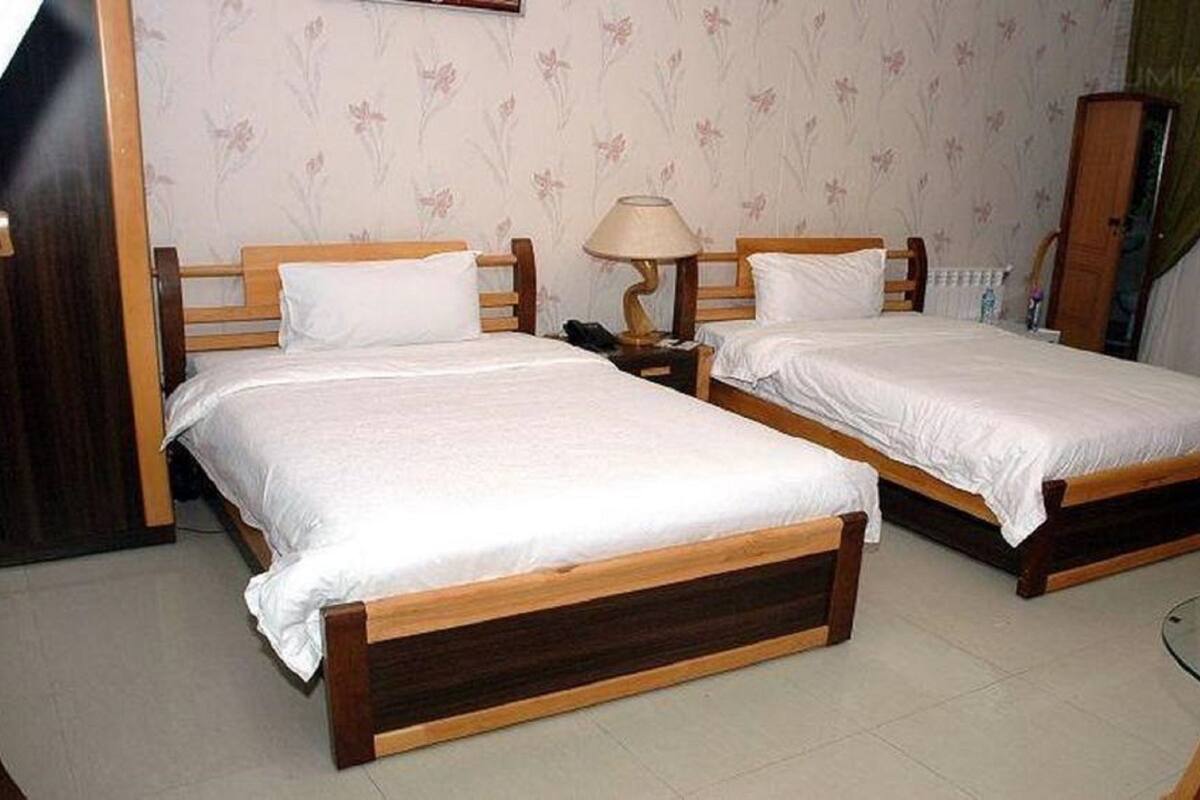 Ein Schlafzimmer mit zwei Holzbett, weißer Bettwäsche, einer Lampe und einem Glastisch.