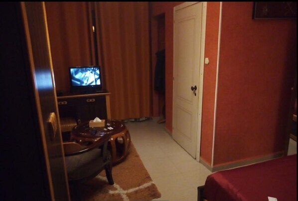 Habitación de hotel con televisión sobre un soporte de madera, una mesita con una silla y una puerta con cerradura.