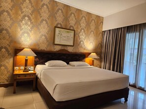 Une chambre d’hôtel avec un grand lit, deux lampes de chevet, un tableau encadré au mur et une fenêtre avec des rideaux.