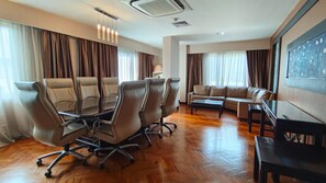 Ein Konferenzraum mit einem langen Tisch, sechs Stühlen, einer Couch und einem Fernsehbildschirm.