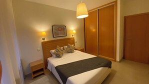 A bedroom with a bed, bedside lamps, a nightstand, a wooden wardrobe, and a ceiling light. - Villas Mare Residence (Nazaré)