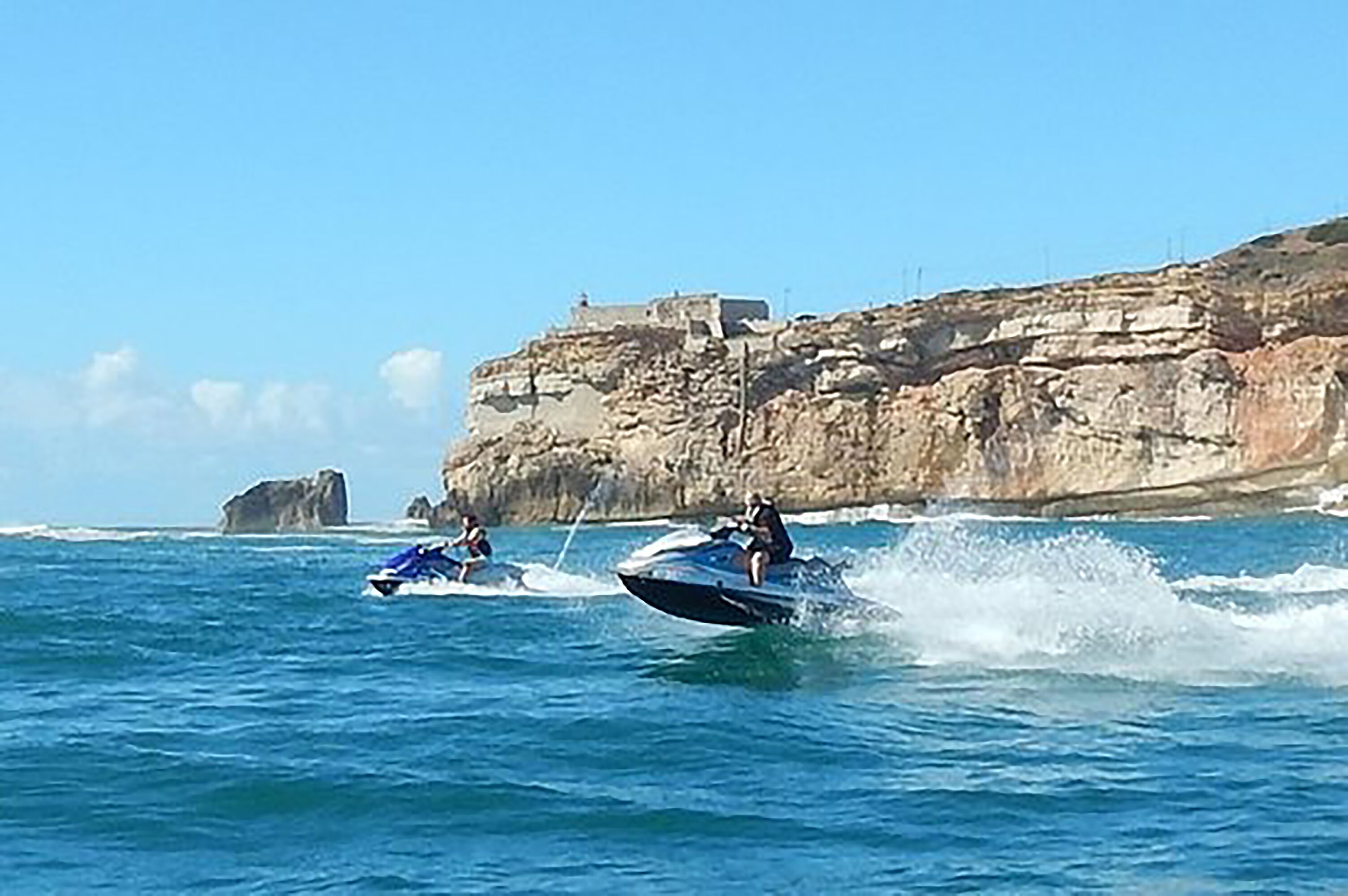 Deux jet-skis sur une étendue d’eau, avec des falaises rocheuses en arrière-plan.