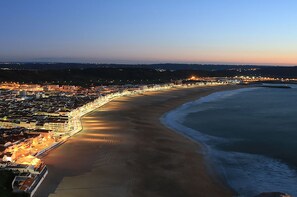 Vista aérea de una ciudad costera con una extensa playa, edificios iluminados y cielo despejado.