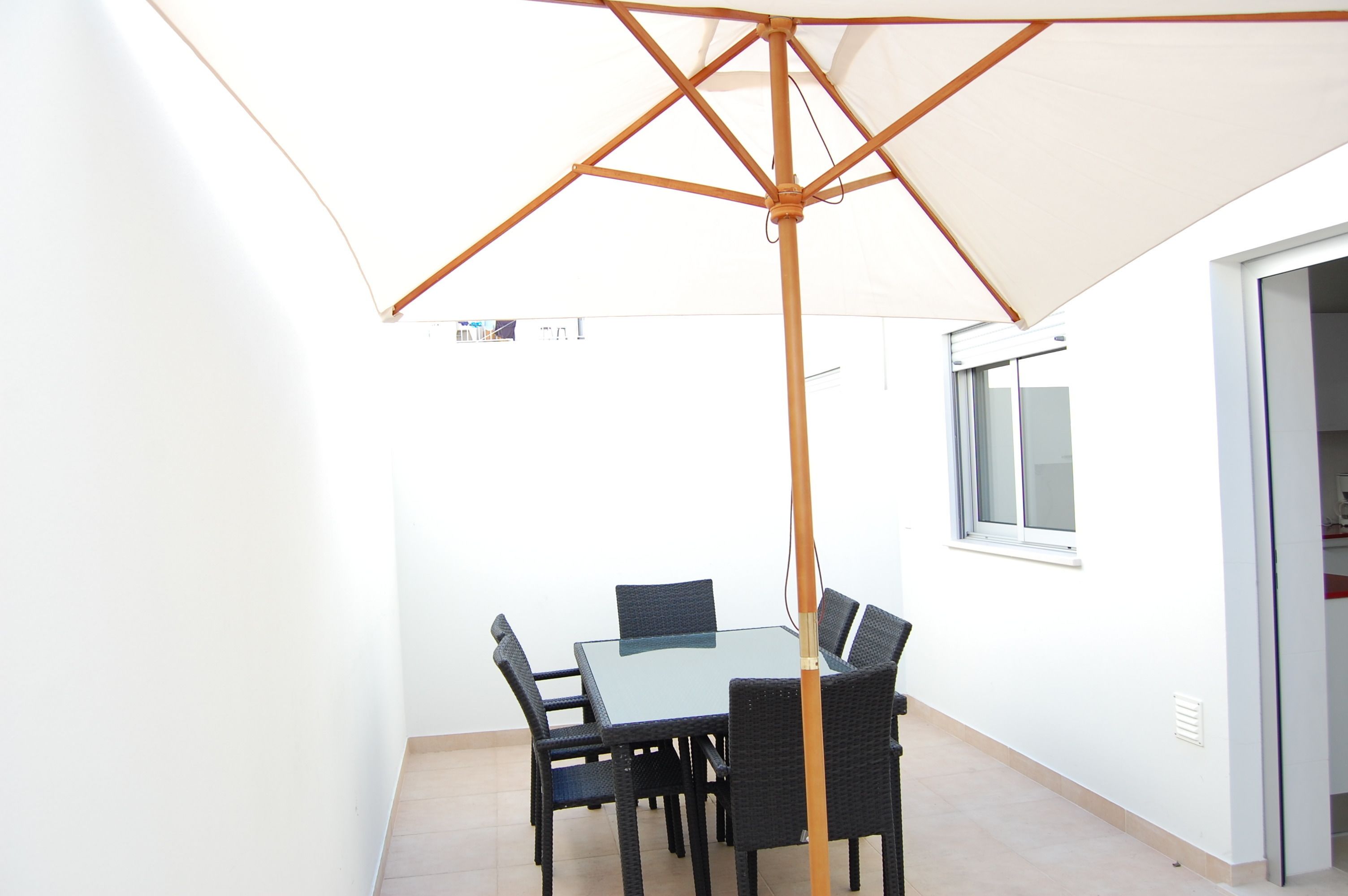 A dining area with a glass table and chairs, a large umbrella, and a window.