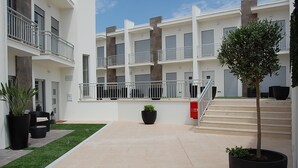 A modern multi-story building with balconies, a central staircase, and potted plants. - Villas Mare Residence (Nazaré)