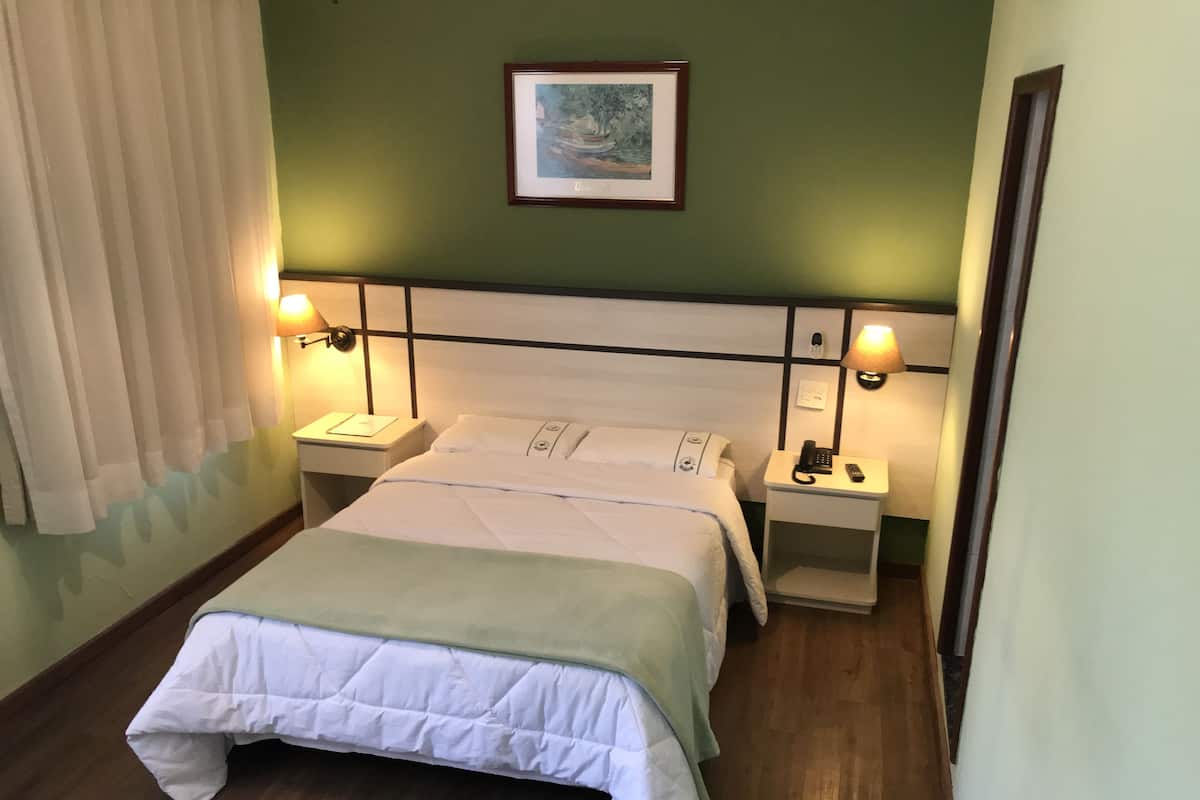 A neatly made bed with a green blanket, two bedside tables with lamps, a framed picture on the wall, and a wooden floor.