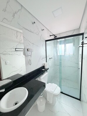A modern bathroom with a marble wall, a black countertop, a white sink, a toilet, and a glass-enclosed shower.
