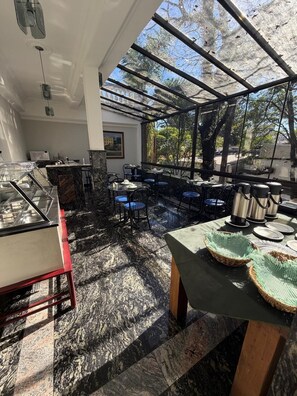 A restaurant with a glass enclosure, marble flooring, and outdoor seating with chairs and tables.