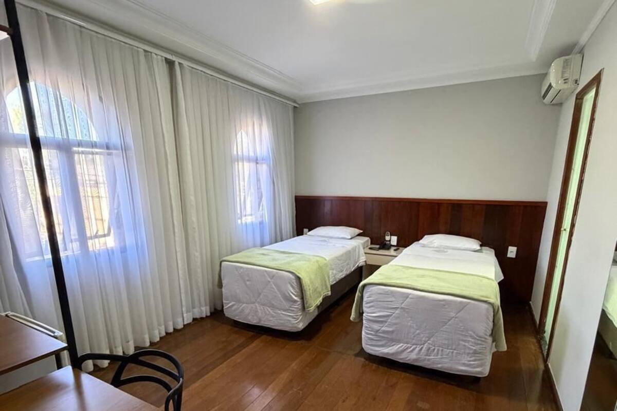 A hotel room with two beds, a desk, a chair, and a window with curtains.