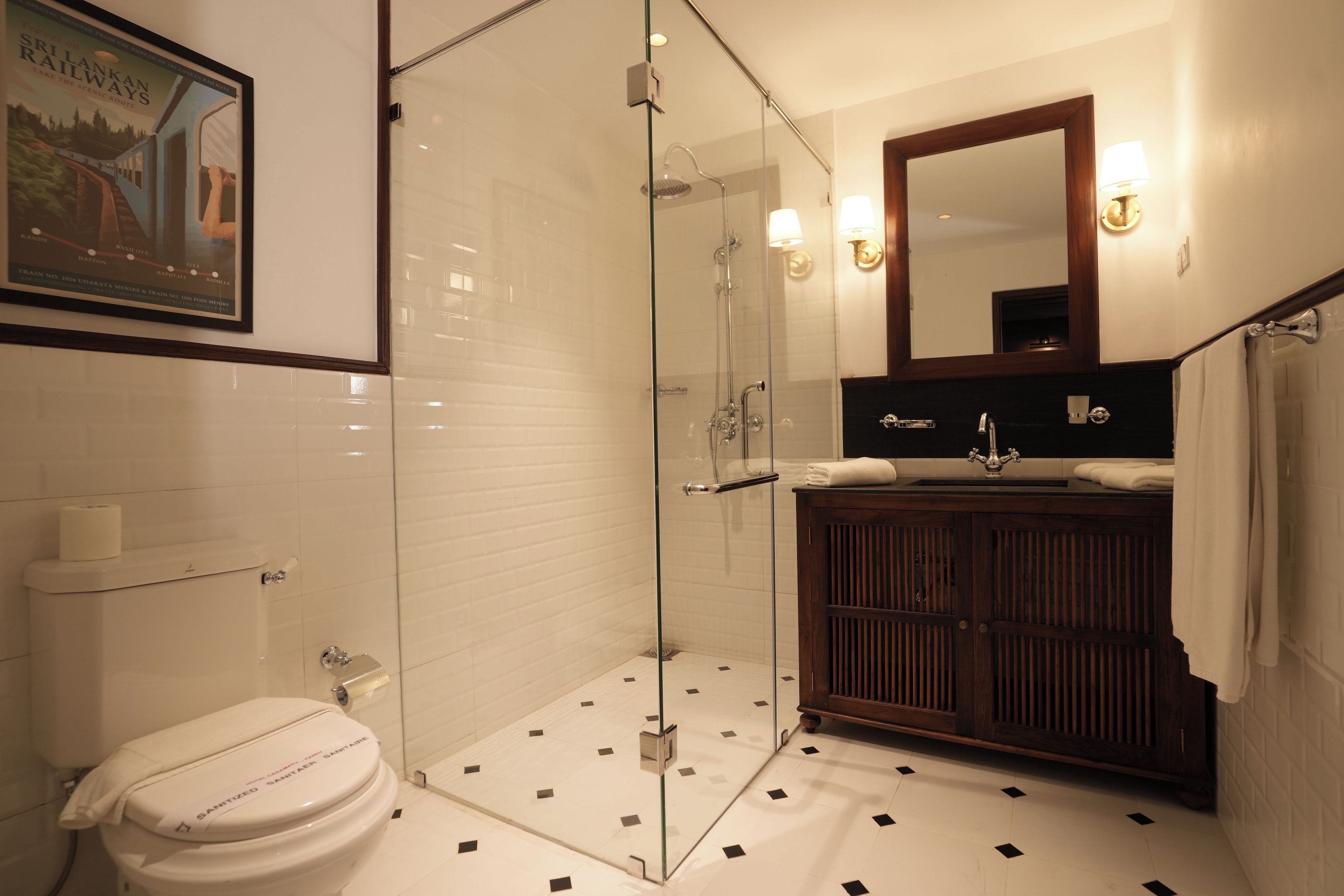Un bagno con doccia vetrata, un WC bianco, un mobile bagno in legno con specchio e un quadro appeso al muro.