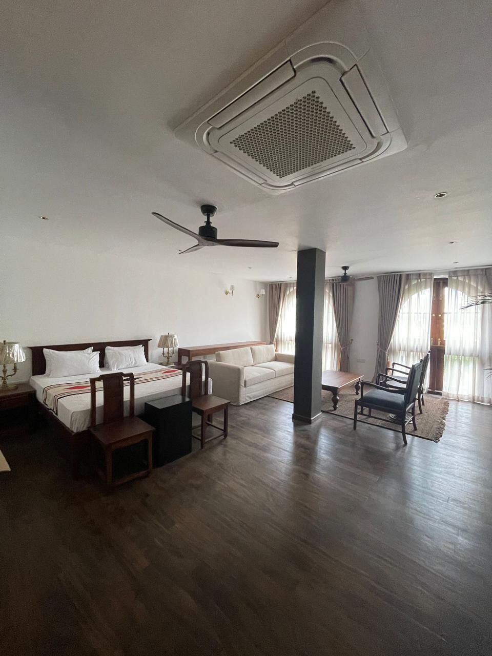 A hotel room with a bed, a sofa, a dining table, and a ceiling fan.