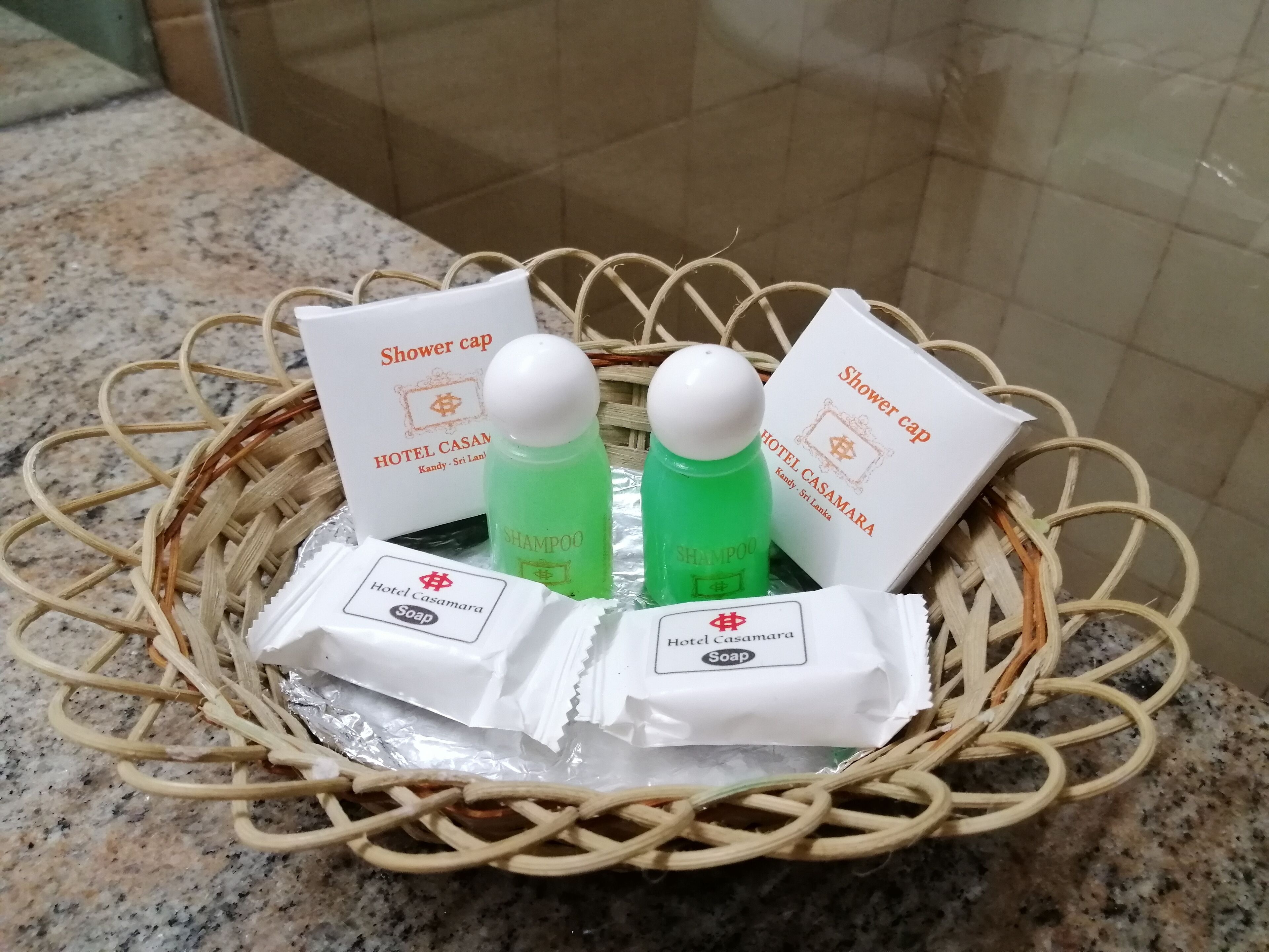 A wicker basket containing hotel amenities including shower caps, shampoo, and soap.