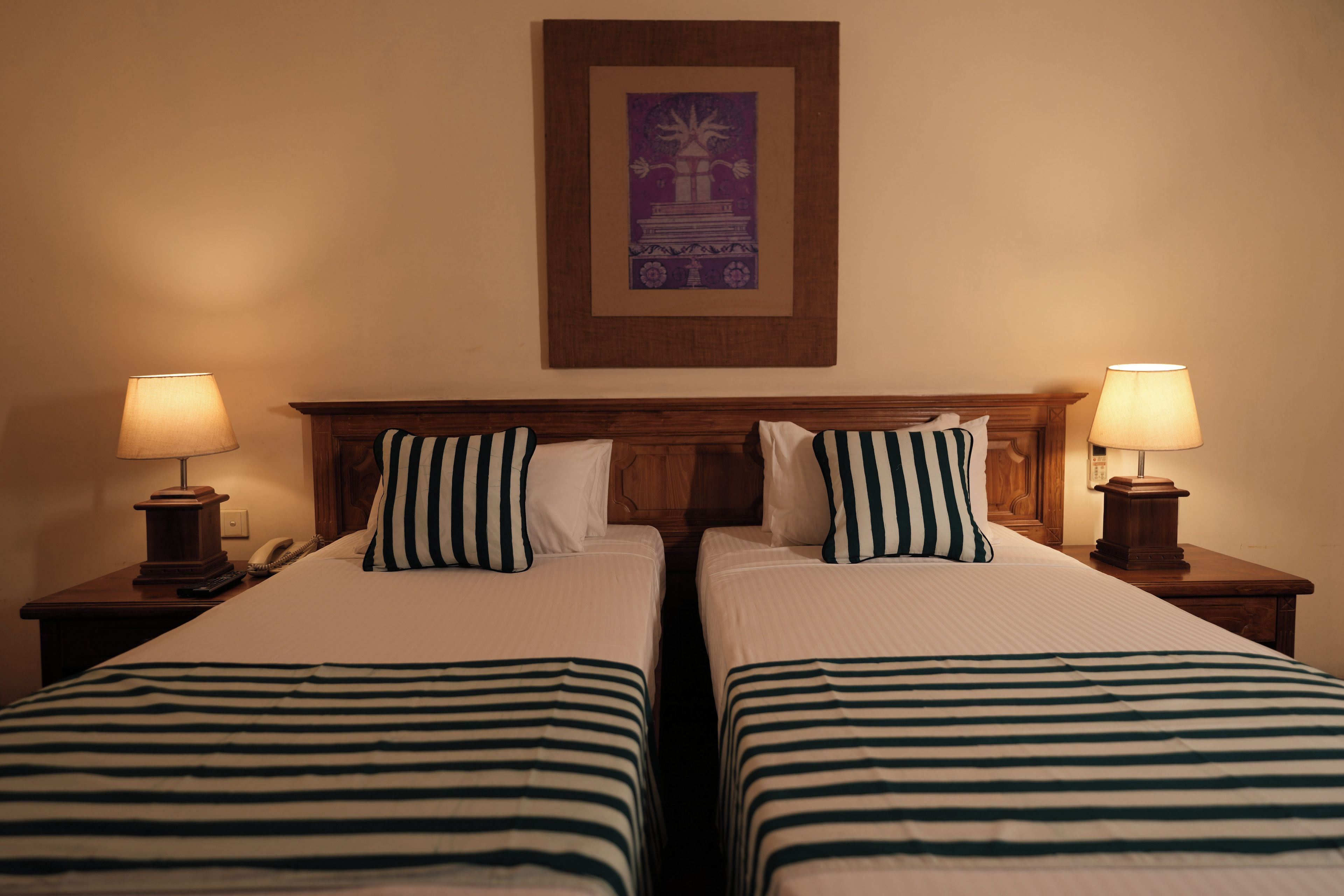 A hotel room with two beds, each with a striped bedspread, a wooden headboard, and two bedside lamps.