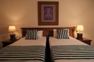 A hotel room with two beds, each with a striped bedspread, a wooden headboard, and two bedside lamps.