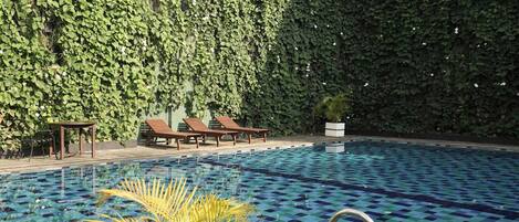 Una piscina con diseño de cuadros, rodeada por un muro verde exuberante y sillones de descanso.