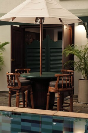A poolside seating area with a table and chairs, a pool, and a door with shutters. - Hotel Casamara (Kandy)