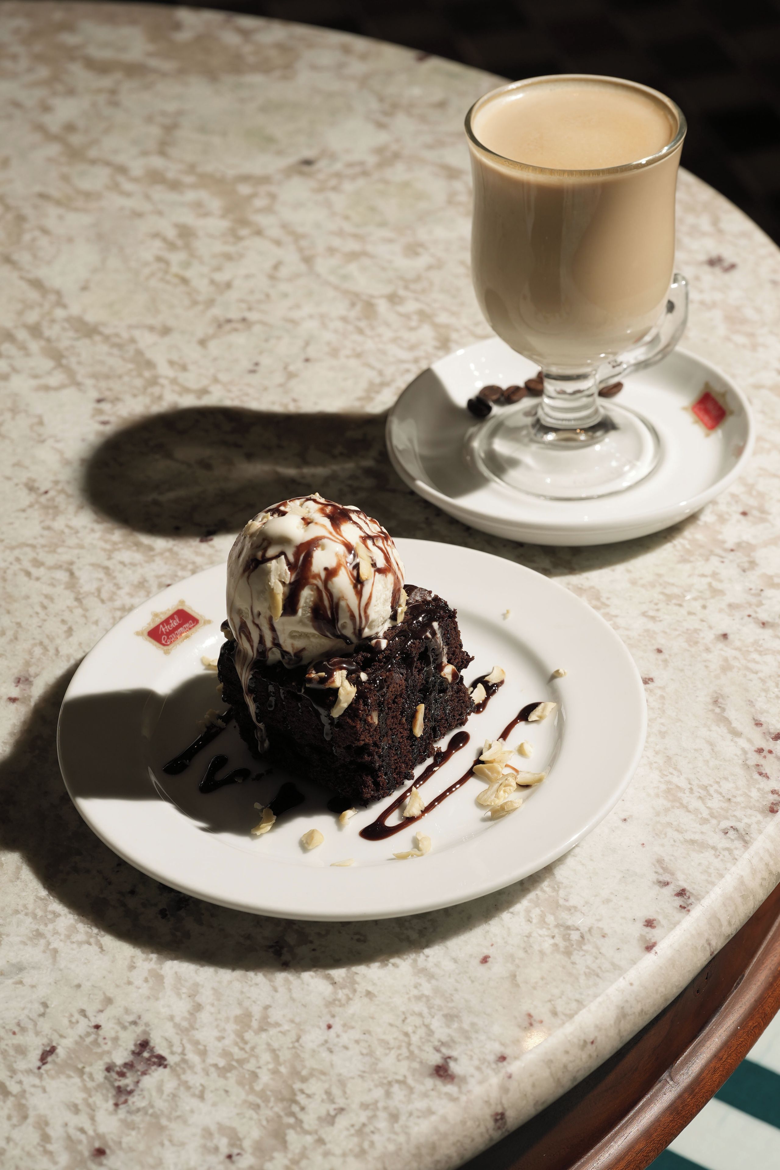 Un plato de postre con pastel de chocolate y helado, acompañado de una taza de café sobre una mesa de mármol.