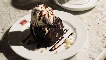 Un plato de postre con pastel de chocolate y helado, acompañado de una taza de café sobre una mesa de mármol.
