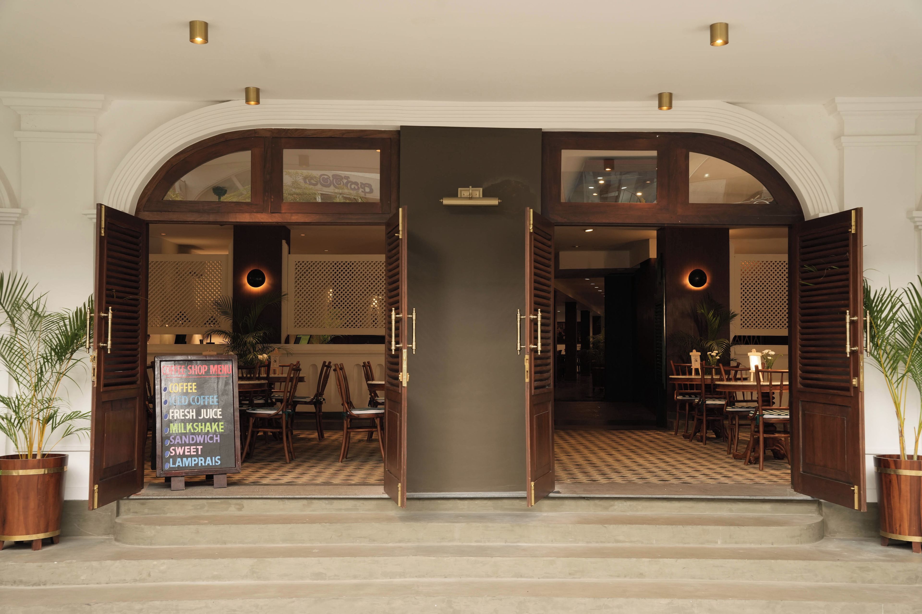 L’entrée d’un hôtel avec un sol à carreaux, un panneau affichant le menu d’un café, et des portes en bois.