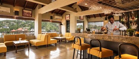 A bar area with yellow seating, a bartender preparing drinks, and a view of the city through large windows.