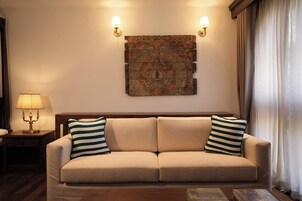 A living room with a beige sofa, striped pillows, a wooden side table with a lamp, and a wall-mounted artwork.