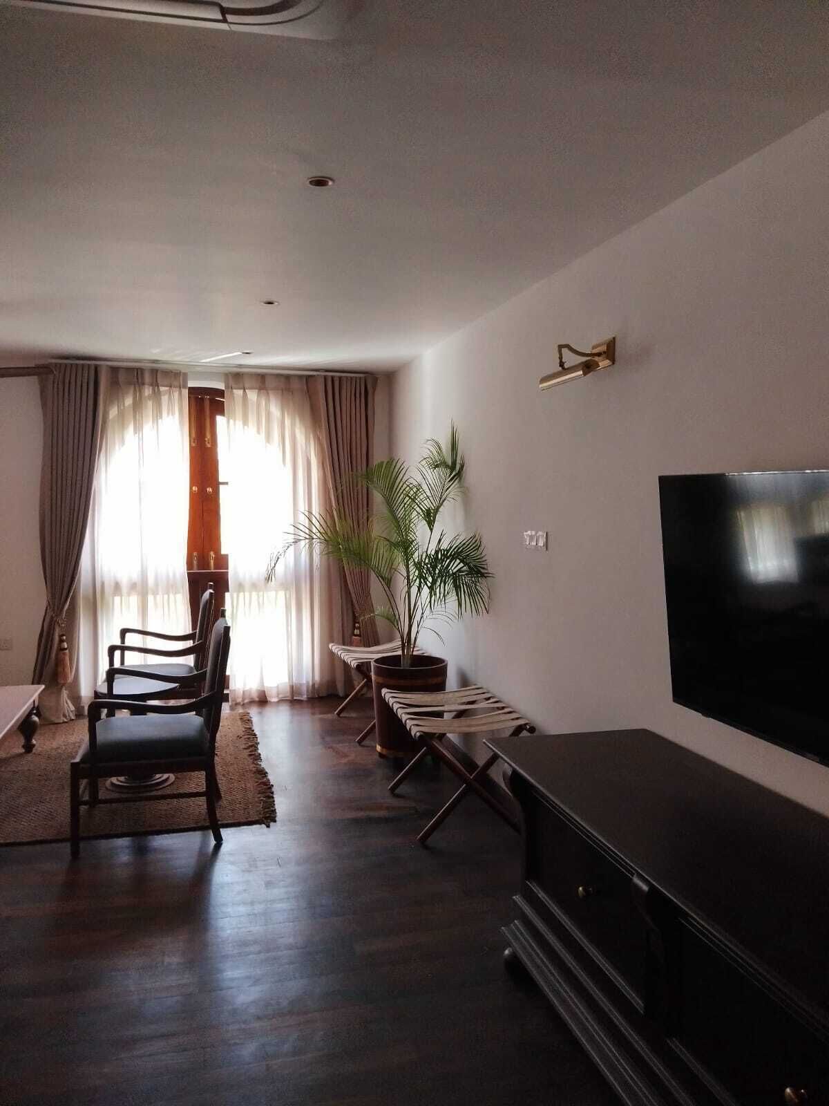 Una sala de estar con televisión de pantalla plana, piso de madera oscura, un comedor con sillas y una planta grande en maceta.