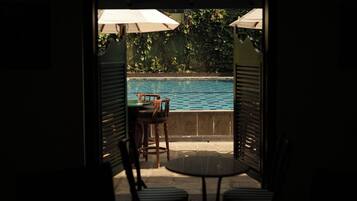 Un área de estar al aire libre con vista a la piscina, que incluye una mesa y sillas bajo sombrillas.