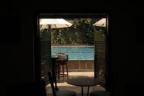 An outdoor seating area with a pool view, featuring a table and chairs under umbrellas. - Hotel Casamara (Kandy)