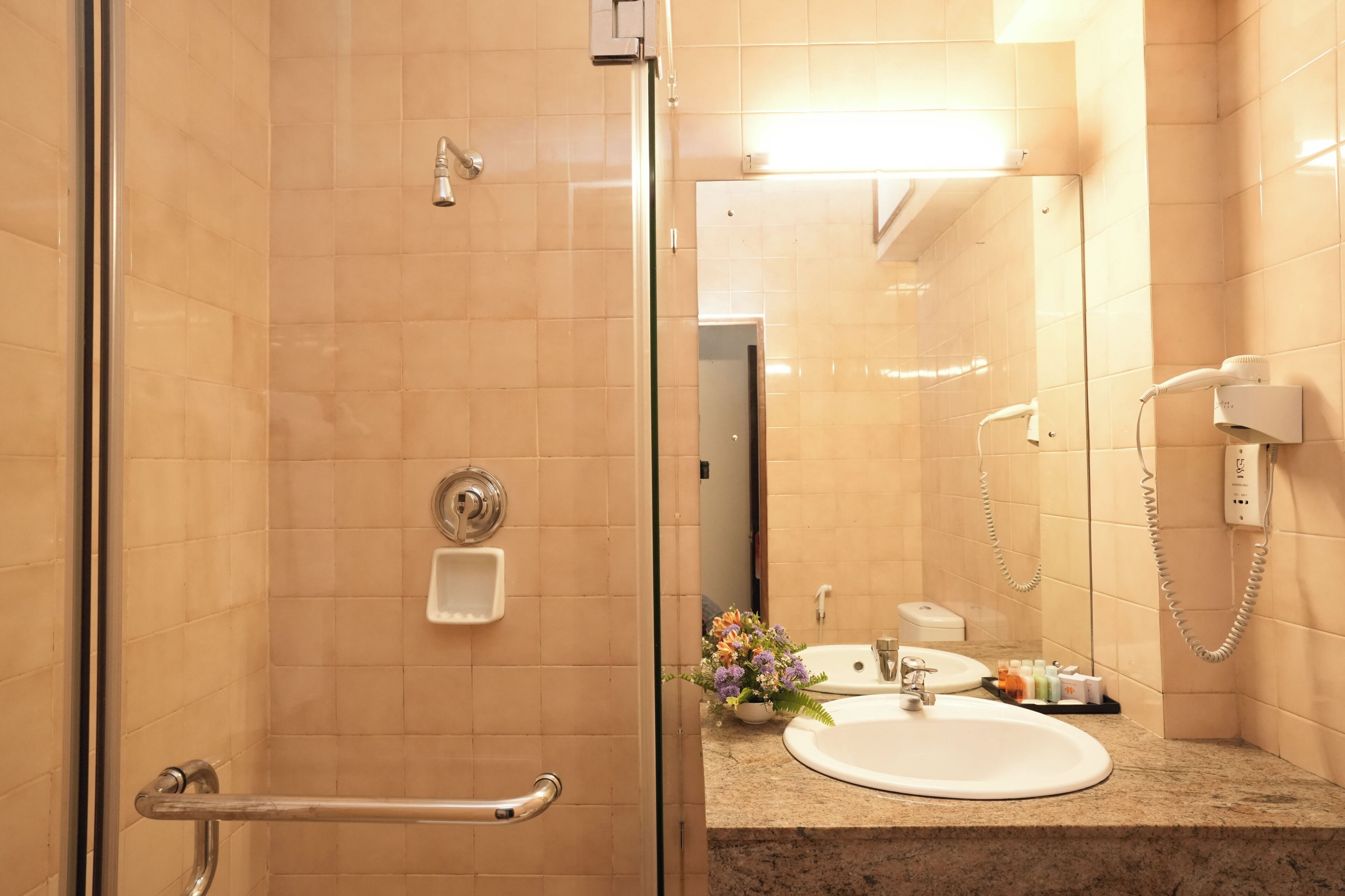 Een badkamer met een douchecabine van glas, een wastafel met spiegel en een telefoon.